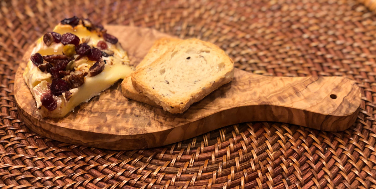 Olive wood board with cheese and bread on a woven placemat