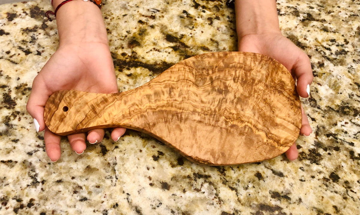 Hands holding the olive wood board, showing its grain