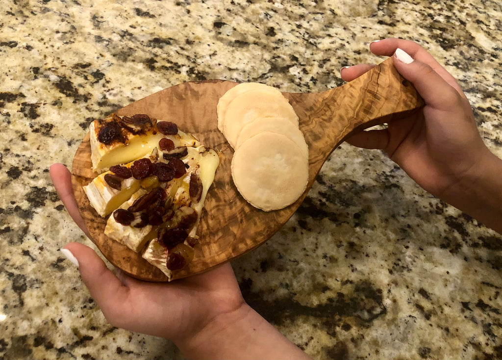 Olive wood board held by its handle with cheese